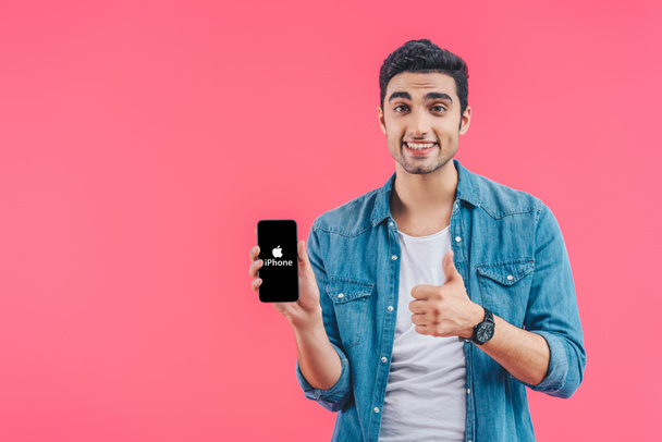 happy young man doing thumb up gesture and showing iphone smartphone isolated on pink - Foto, Bild