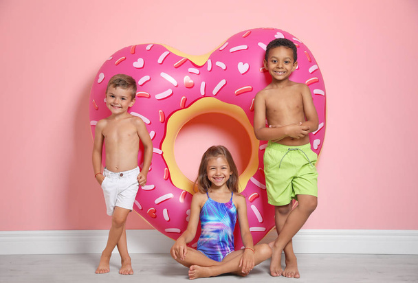 Cute little children with bright heart shaped inflatable ring near color wall - Φωτογραφία, εικόνα