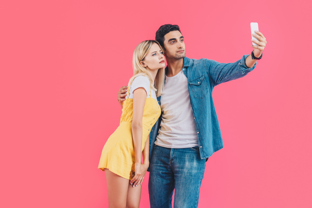 serious young couple taking selfie on smartphone isolated on pink  - Foto, immagini
