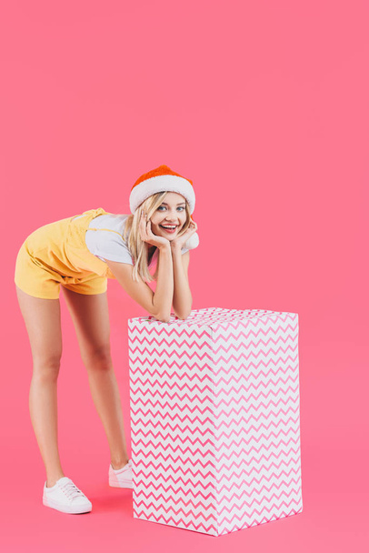 jeune femme souriante dans le chapeau de Noël debout avec une grande boîte cadeau isolé sur rose
 - Photo, image