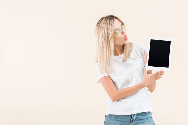 yllättynyt tyylikäs nainen silmälasit näytetään digitaalinen tabletti tyhjä näyttö eristetty beige
 - Valokuva, kuva