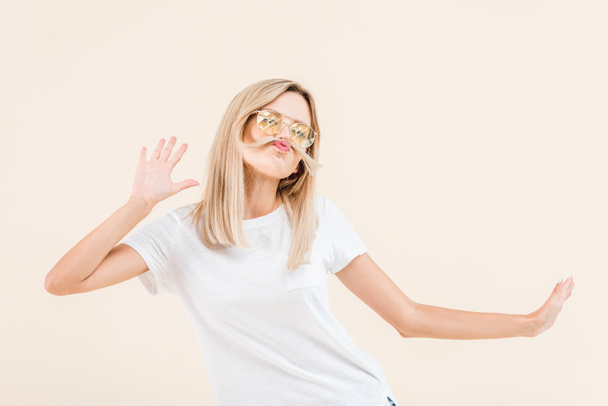 giovane donna bionda in occhiali da sole divertirsi con i capelli isolati su beige
  - Foto, immagini