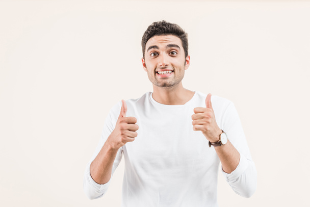 happy young man showing thumbs up and smiling at camera isolated on beige  - Foto, Imagen