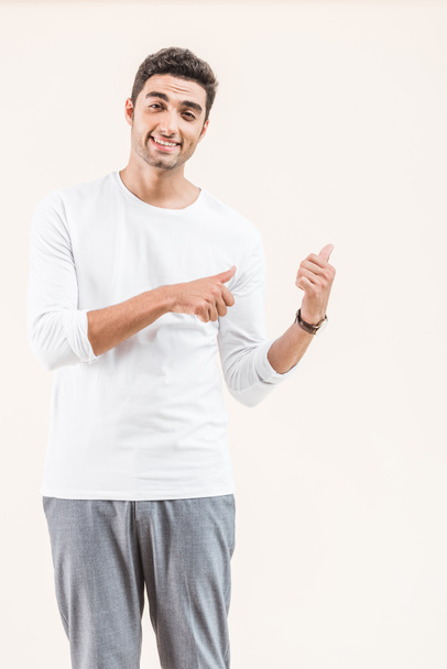 handsome young man pointing at copy space and smiling at camera isolated on beige - Foto, afbeelding
