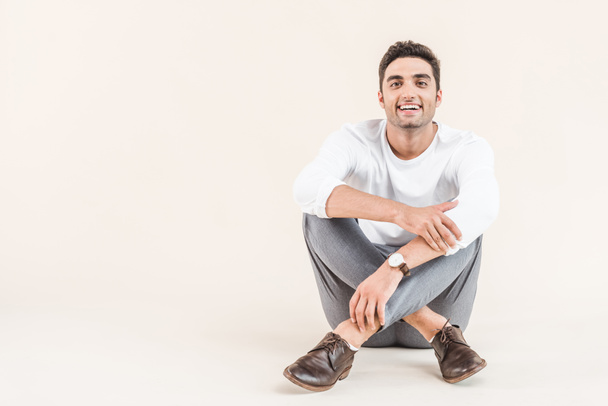 cheerful young man sitting and smiling at camera isolated on beige - Photo, Image