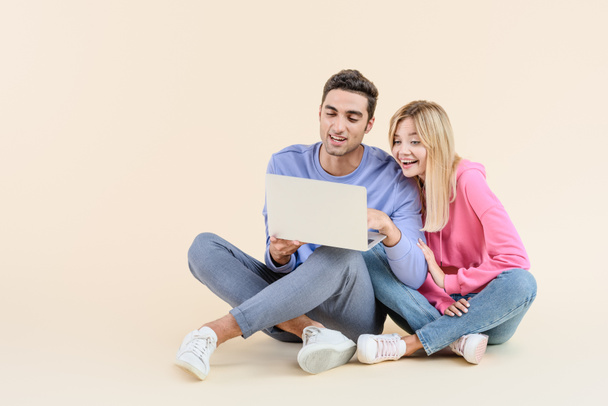 felice giovane coppia seduta insieme e utilizzando computer portatile isolato su beige
 - Foto, immagini