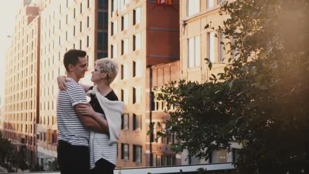Beautiful young romantic couple standing and hugging on an amazing New York sunset bridge, urban buildings background. - Кадри, відео