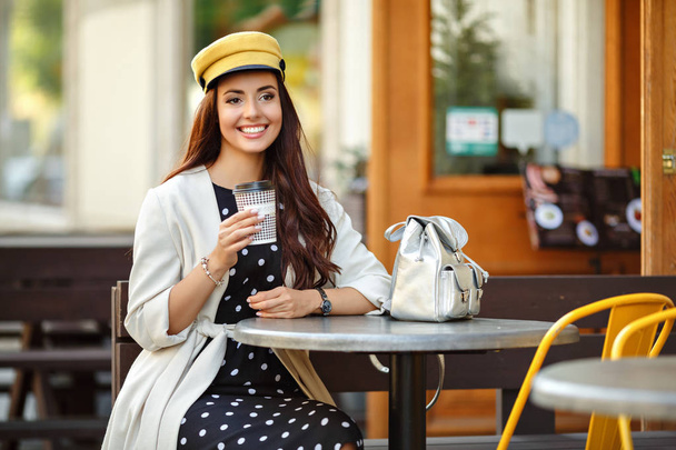 Beautiful, glamorous and stylish brunette girl sits in a street cafe in the city and smiles. Street Style - Photo, image