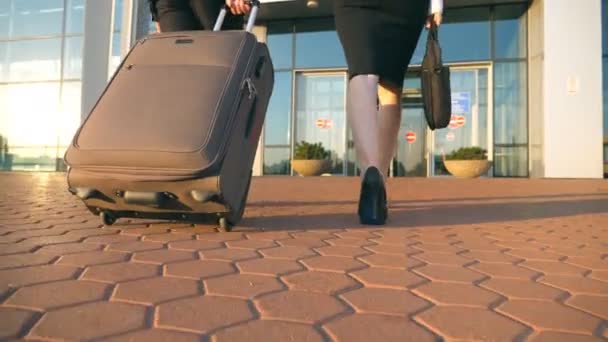 Business man and woman going to the airport with their luggage. Young businessman carrying suitcase on wheels and walking with his female colleague to terminal hall. Trip or travel concept Slow motion - Footage, Video