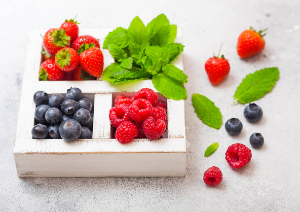 Fresh raw organic berries in white wintage wooden box on kitchen table background.  Strawberry, Raspberry, Blueberry and Mint leaf - Zdjęcie, obraz
