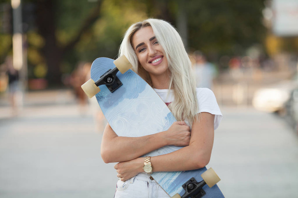 beautiful girl with skateboard. girl holding a skateboard in hands. Longboard in the hands of a girl in a jeans shorts. Girl in the park with longboard in the hand - Fotoğraf, Görsel