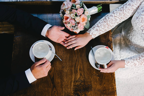 Wedding couple at cafe, top view. Man and woman's hands and coffee cups on the table - Fotó, kép