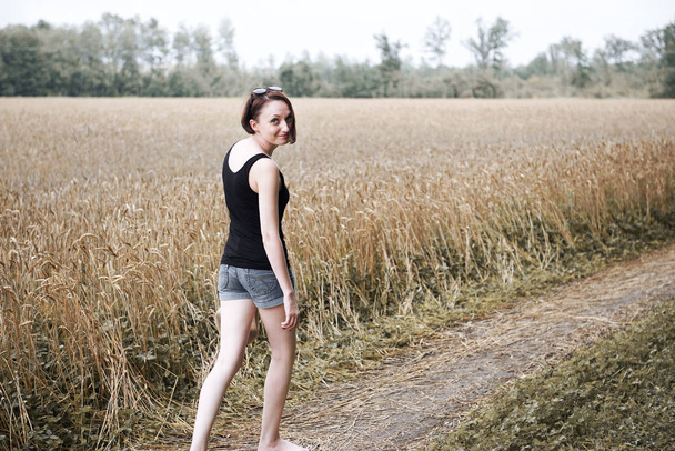 νεαρή κοπέλα περπάτημα χωρίς παπούτσια στο έδαφος δρόμο μέσα από το πεδίο και δάσος, η έννοια του καλοκαιριού και ταξίδια - Φωτογραφία, εικόνα