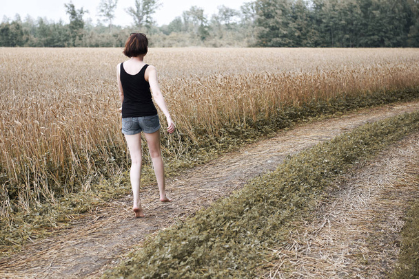 junges Mädchen, das barfuß auf dem Feldweg durch Feld und Wald läuft, das Konzept von Sommer und Reisen - Foto, Bild