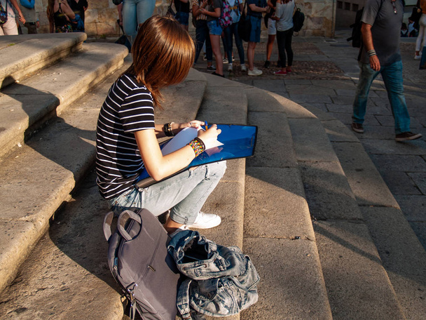 Una adolescente escribiendo con un bolígrafo en un folio en una carpeta sentada en las escaleras de un campus universitario
 - Foto, Imagen