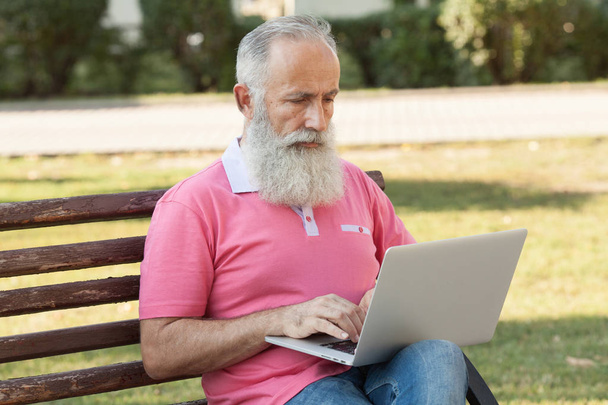 Senior man using laptop computer at rest in the park outdoors - Fotó, kép