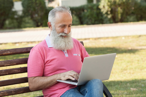 Senior man using laptop computer at rest in the park outdoors - 写真・画像