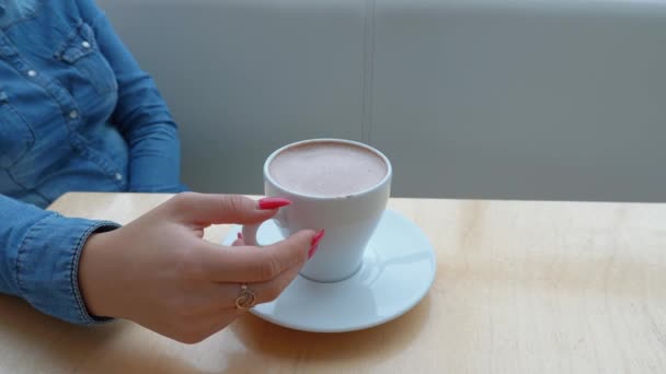 Chica en una camisa de mezclilla azul sostiene una taza de café blanco en un café
 - Metraje, vídeo