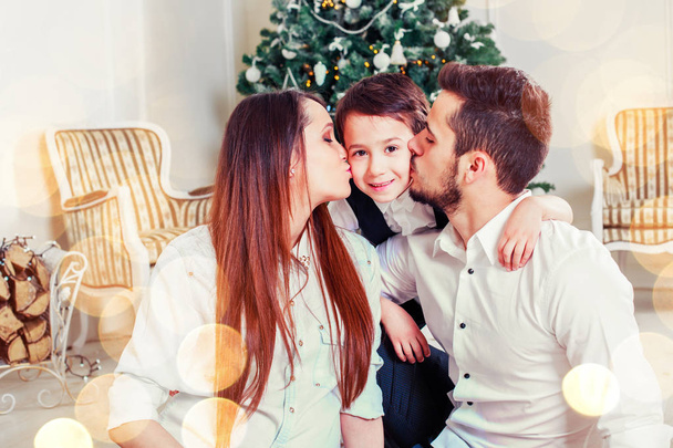 Jouluperhe hymyilee ja suutelee joulukuusen lähellä. Olohuone koristeltu joulukuusi ja läsnä lahjapakkauksessa, valo antaa viihtyisä tunnelma. Uusi vuosi teema
 - Valokuva, kuva