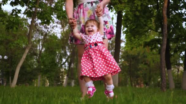 赤ちゃんはママの手と笑いの空気で回転しています。小さな娘が遊んで彼女の母春の公園の緑の草の上. - 映像、動画