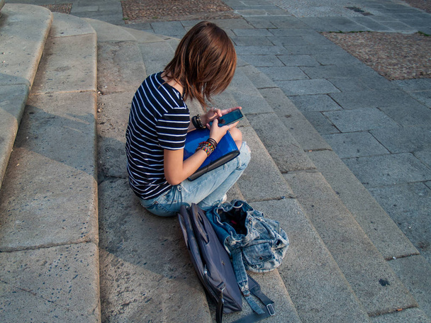 Une adolescente avec un téléphone intelligent sur les mains dans les escaliers d'un bâtiment historique
 - Photo, image