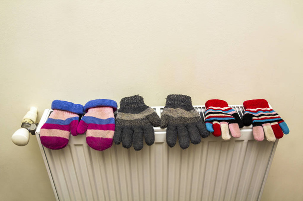 Kinderwarme handgestrickte gestreifte Wollhandschuhe, die nach dem Wintertag draußen auf dem Heizkörper trocknen - Foto, Bild