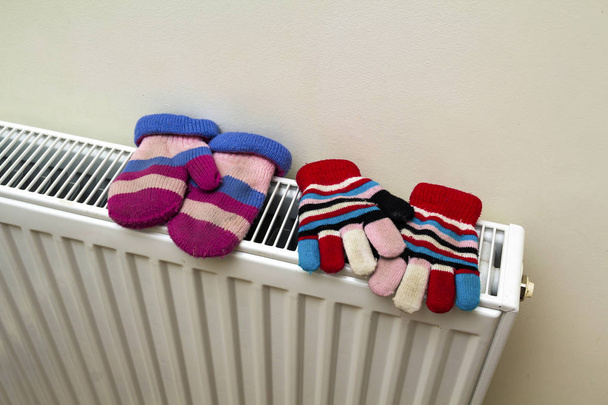 Guantes de lana rayados de punto a mano calientes de los niños que se secan en el radiador de calefacción después del día de invierno afuera
 - Foto, imagen