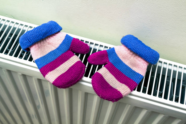 Kinderwarme handgestrickte gestreifte Wollhandschuhe, die nach dem Wintertag draußen auf dem Heizkörper trocknen - Foto, Bild