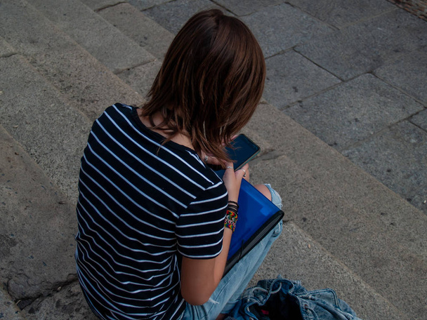 Una adolescente con un teléfono inteligente en las manos en las escaleras de un edificio histórico
 - Foto, Imagen