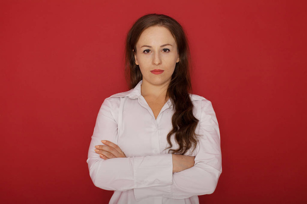 Charming businesswoman. Confident young businesswoman keeping arms crossed and looking at camera while standing against red background - Foto, Bild