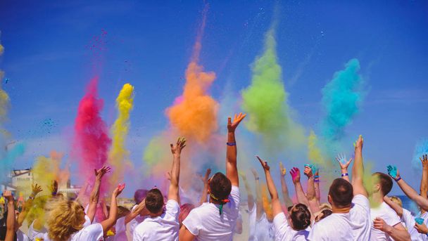 яркие люди празднуют праздник Холи, группа людей бросают краски в голубое небо
. - Фото, изображение