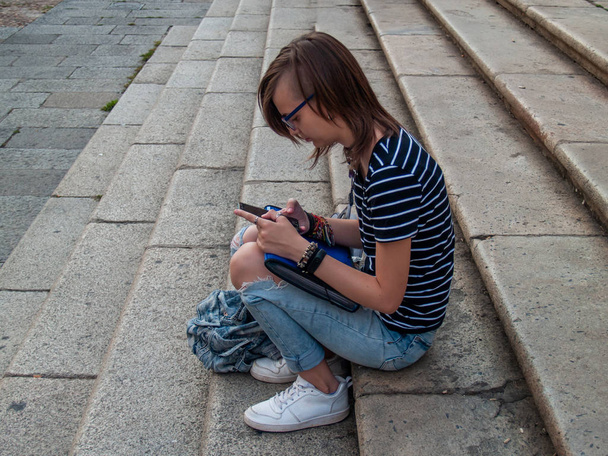 Een tiener vrouw met een slimme telefoon op haar handen op de trappen van een historische gebouw - Foto, afbeelding