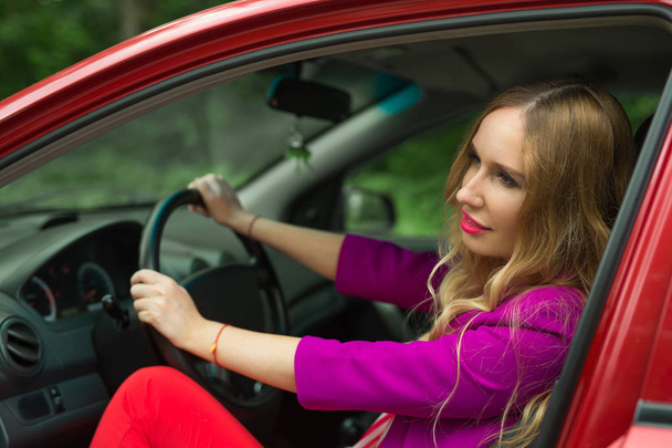 beautiful young girl in a jacket driving a red car - 写真・画像