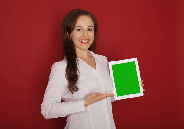 Portrait with copy space empty place of pretty charming confident trendy woman in classic shirt having tablet in hands looking at camera isolated on red background - Fotó, kép