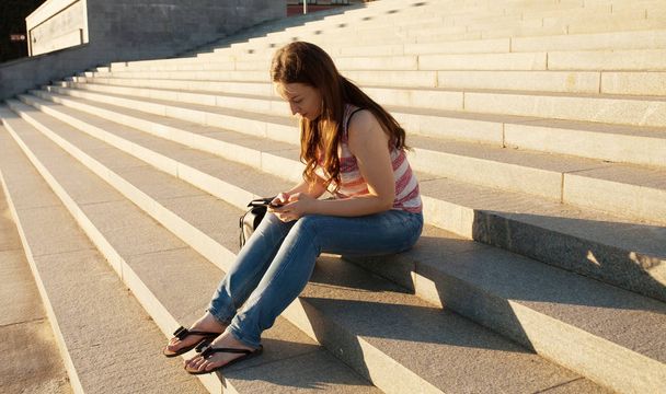 Image of beautiful stylish woman sitting on street stairs on summer day and holding mobile phone - Foto, Bild