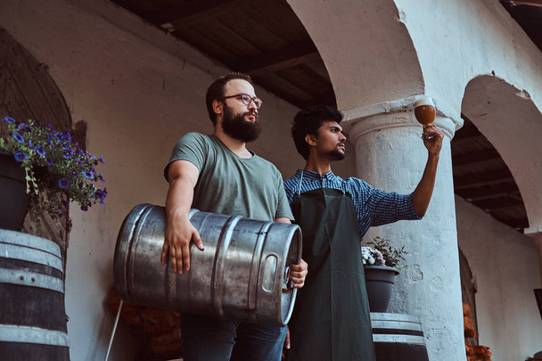 Two brewers in apron standing outdoors checking the quality of brewed drink at brewery factory. - Photo, Image