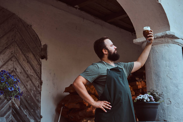 Эксперт-пивовар по фартуку стоит на улице и проверяет качество варки на пивоваренном заводе
. - Фото, изображение