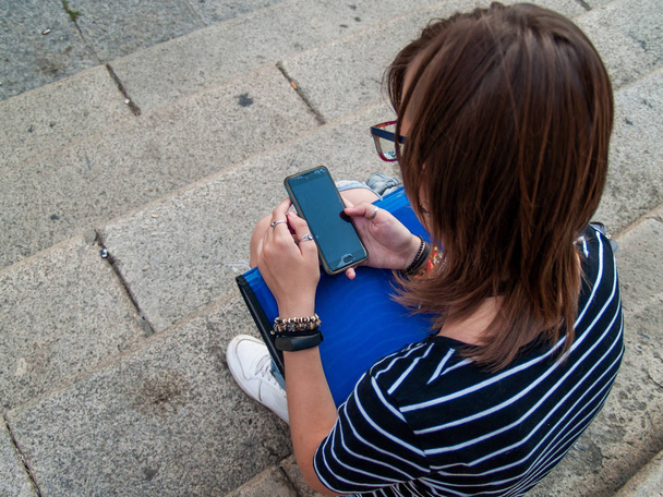Μια Έφηβη γυναίκα με ένα έξυπνο τηλέφωνο σχετικά με τα χέρια της στις σκάλες του ένα ιστορικό κτίριο - Φωτογραφία, εικόνα