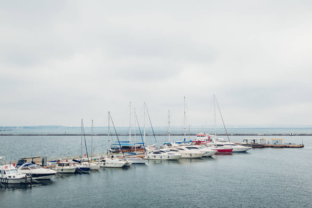 Yachts moored in on pier of seaport on rainy day. Row of boats in Odesa - Фото, изображение