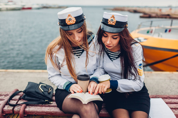 Two college women students of Marine academy reading book by sea wearing uniform. Friends studying by coast - Photo, Image