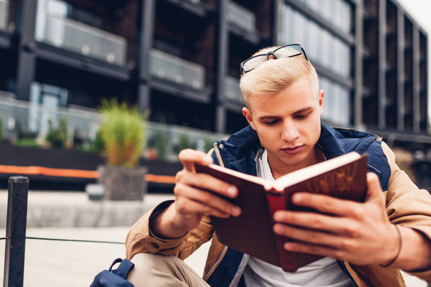 Студент колледжа с рюкзаком читает книгу охлаждения в современном отеле в дождливый осенний день. Концепция образования
 - Фото, изображение