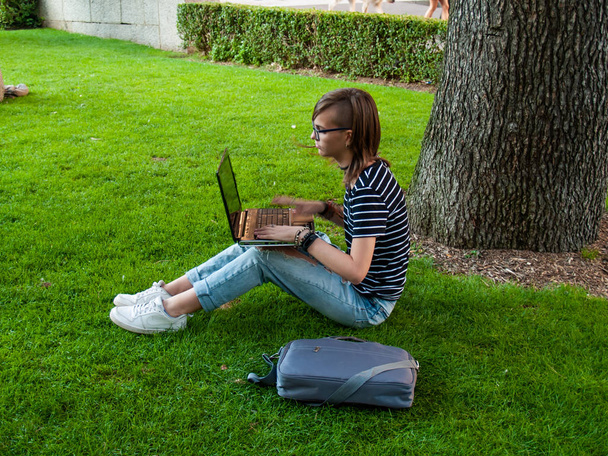 Una adolescente que estudia con un portátil sentado en el césped en un parque de una universidad en un campus universitario
 - Foto, imagen