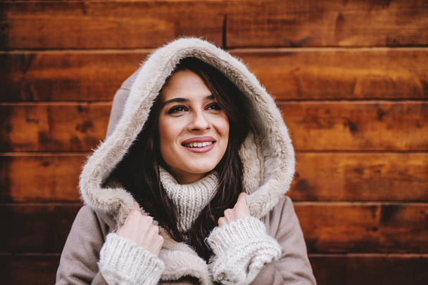 happy beautiful woman in winter coat against wooden wall - Фото, изображение