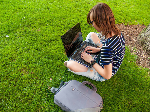 Una adolescente que estudia con un portátil sentado en el césped en un parque de una universidad en un campus universitario
 - Foto, Imagen