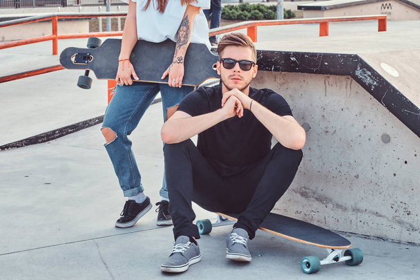 Portret stylowy hipster facet siedzi na longboard o skatepark. - Zdjęcie, obraz