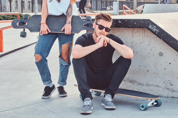 Portrait of a stylish hipster guy sitting on a longboard at a skatepark. - Zdjęcie, obraz