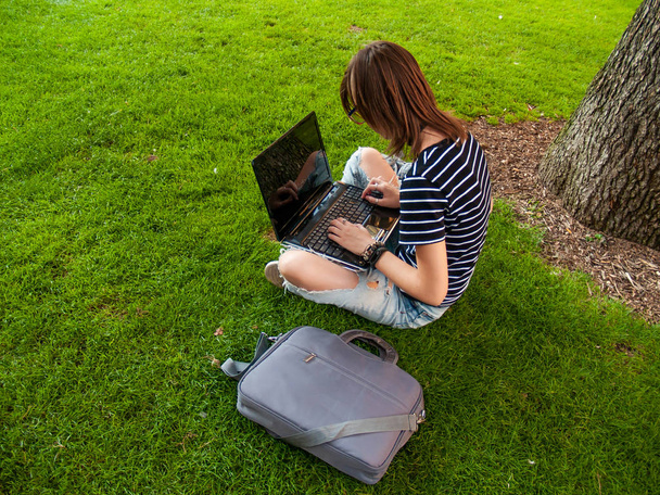 Uma adolescente estudando com um laptop sentado na grama em um parque de uma universidade em um campus universitário
 - Foto, Imagem