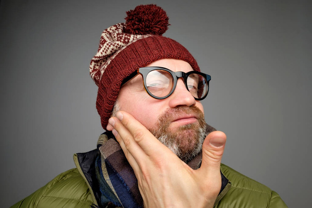 Legrační zralý muž nosí brýle a teplé oblečení, při pohledu na fotoaparát kontrola jeho štětin. Je to velmi pohodlné mít vousy v zimní době - Fotografie, Obrázek