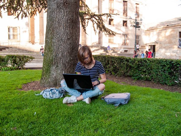大学のキャンパスで大学の公園の草の上に座ってノート パソコンを勉強して 10 代の女性 - 写真・画像