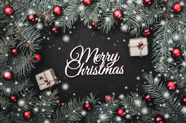 Ευχετήρια κάρτα Χριστουγέννων σε μαύρο φόντο. πλαίσιο των υποκαταστημάτων έλατο στολισμένο με κόκκινες μπάλες. Εφέ χιόνι και διακοσμητικά δώρα - Φωτογραφία, εικόνα